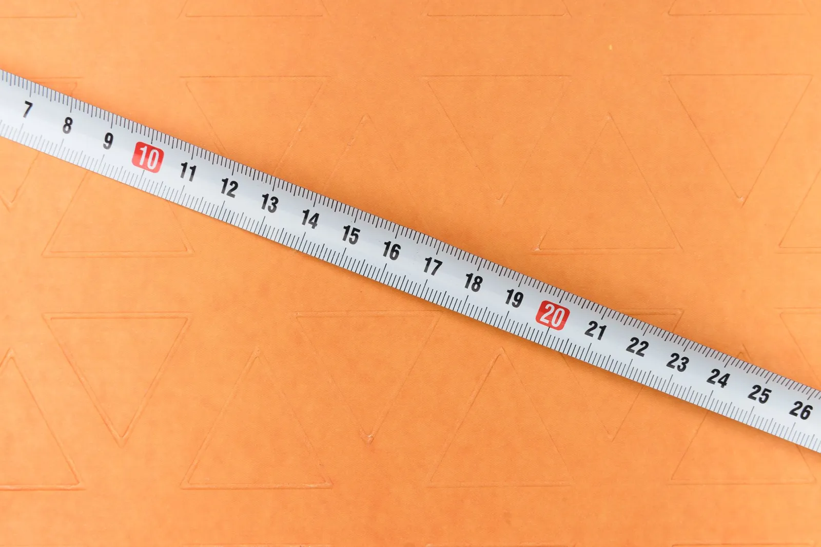 주황색 바탕 위에 10과 20 눈금이 빨갛게 표시된 흰색 줄자를 비스듬히 놓은 정물 사진 — 담낭 용종은 몇 mm인지가 다음 단계를 정하는 기준이 된다는 맥락