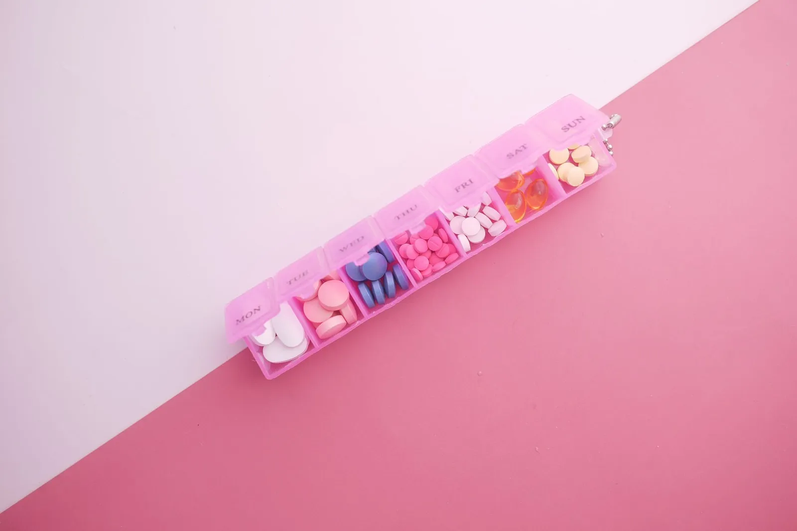 분홍 배경 위에 놓인 요일별 알약 정리함 정물 — 몇 년째 매일 먹는 약이 있다면 비타민 B12 흡수를 줄이는 약인지 한 번 살펴볼 맥락